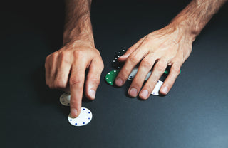 Hands arranging poker chips on a dark surface.